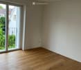 Empty room with wooden flooring, large sliding glass doors leading to a balcony, and white walls.