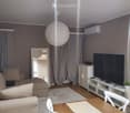 A modern living room with a sofa, a wooden dining table, white chairs, a television on a cabinet, a large round ball lamp, and a mirror leading to another room.