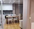 Open-plan living and dining area with light wooden flooring, white cabinets, a sofa, a dining table with chairs, and a microwave in the kitchen area.