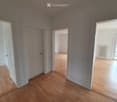Empty room with wooden flooring, white walls, and multiple doors leading to other spaces.