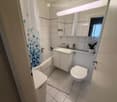 Modern bathroom with white tiles, bathtub, sink, toilet, mirror, and a small plant on the counter.