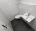 Modern bathroom with white tiled walls, dark grey tiled floor, toilet, and a white sink with a chrome faucet.