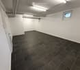 Empty room with white walls, dark tiled floor, and a small window. No furniture or equipment present.