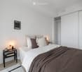 Modern bedroom with a neatly made bed, nightstand, lamp, and a picture frame on the wall.