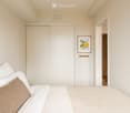A modern bedroom with a neatly made bed, white bedding, a brown throw pillow, a built-in wardrobe, and a framed picture of lemons on the wall.