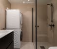 Modern bathroom with a white sink, black faucet, mirror, glass-enclosed shower, and a stacked washer/dryer unit.