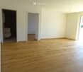 Empty room with wooden flooring and white walls, featuring two doorways leading to other rooms.
