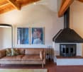 Living room with exposed wooden beams, a tan leather sofa with patterned pillows, a floor lamp, and a fireplace with artwork above it.