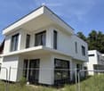 Modern two-story white house with large windows and a flat roof, featuring a balcony on the upper level.