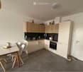 Modern kitchen with light wood cabinets, stainless steel appliances, and a small dining area with a table and chairs.