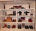 A neatly organized display cabinet filled with various pairs of shoes, decorative vases, framed pictures, and boxes, arranged on multiple white shelves.