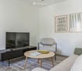 Modern living room with a grey sofa, wooden coffee table, armchair, TV stand, and two picture frames on the wall.