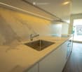 Modern kitchen with marble countertop, stainless steel sink, and sleek white cabinets.