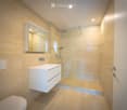 Modern bathroom with light-colored tiles, a white sink with a built-in cabinet, a large mirror, a glass-enclosed shower, and a toilet.
