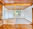 An empty room with wooden walls, a wooden ceiling, and a wooden floor. The room features built-in wooden cabinets and shelves, with large windows allowing natural light to enter.