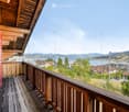 Wooden balcony with railing overlooking a scenic lake and town, with distant mountains visible.