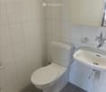 A small, clean bathroom with white tiled walls, a toilet, a sink with a mirror, and a white cabinet above the sink.