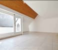 Empty room with white walls, tiled floor, large windows, and a wooden bench in the corner.