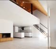 Open-plan living and kitchen area with white walls, a fireplace, a bench, and a staircase leading to an upper level.