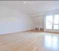 Empty room with wooden flooring, white walls, and large windows with sliding doors leading to a balcony.