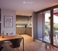 Modern dining area with a wooden table, chairs, and a vase of flowers. The space is connected to a sleek kitchen with cabinets and a countertop. Large sliding glass doors open to a patio with outdoor furniture.