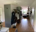 A well-lit hallway with wooden flooring, coat rack, and a cat tree in the background.