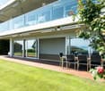 Well-maintained garden with a wooden deck, outdoor dining set, and modern house with large glass windows and balconies.
