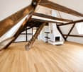 Empty attic space with wooden beams, polished wooden floor, and a white fireplace with a tiled surround.