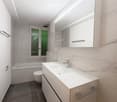 Modern bathroom with a white sink, mirror, bathtub, and toilet. The walls are tiled in a marble pattern, and the floor is dark grey tiles.