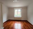 Empty room with wooden flooring, white walls, a window with white frame, and a radiator below the window.