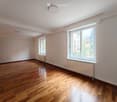 Empty room with wooden flooring, white walls, large windows, and radiators. No furniture or equipment present.