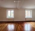 Empty room with wooden flooring, white walls, two windows with radiators, and a simple ceiling light fixture.