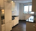 Modern kitchen with white cabinets, stainless steel appliances, dark countertops, and a black tiled floor.