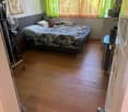 Cozy bedroom with wooden flooring, a bed with a camouflage-patterned blanket, nightstands, a fan, and a curtained window.