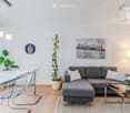 Modern living room with grey sectional sofa, coffee table, dining table with chairs, potted plants, floor lamp, and artwork on the wall.