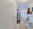 Modern bathroom with white tiled walls and floor, a shower area with a curtain, a sink with a cabinet, a toilet, a towel rack, and a small plant on the windowsill.