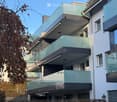 Modern multi-story building with glass balconies and sleek design, featuring multiple levels with large windows and contemporary architecture.
