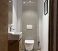 Modern, compact bathroom with a toilet, sink, wooden cabinet, and a framed picture on the wall.