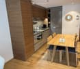 Modern kitchen and dining area with wooden cabinets, a sink, an oven, a dining table with chairs, and a decorative mirror on the wall.