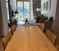Modern living and dining area with a large wooden dining table, chairs, sofa, and a view of the mountains through large windows.