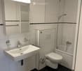 modern bathroom with white tiles, white sink, mirror with light, toilet, bathtub, shower, faucet