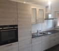 Modern kitchen with light wood cabinets, stainless steel sink, and built-in oven.