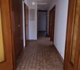 Empty hallway with tiled floor and wooden doors, featuring a ceiling light fixture and a visible electrical outlet on the wall.