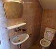 Small bathroom with beige tiles, a sink with a mirror above it, a toilet, and a small shelf holding a glass.
