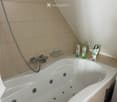 Modern bathroom with a large bathtub featuring multiple jets, a handheld shower hose, a wall-mounted shelf holding toiletries, and a towel draped over the edge.