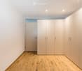 Empty room with light-colored wooden flooring, white walls, built-in closet units, and a small window above the door.