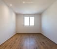 Empty room with wooden flooring, white walls, and a large window with double glass panels.