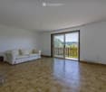 Bright living room with wooden tiled flooring, white walls, a cream-colored sofa, and a sliding glass door leading to a balcony.