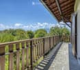 Balcony with wooden railing, overlooking a lush green landscape and distant mountains under a clear blue sky.