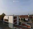 View from a rooftop terrace overlooking a modern apartment building and a traditional village church with a spire in the background.